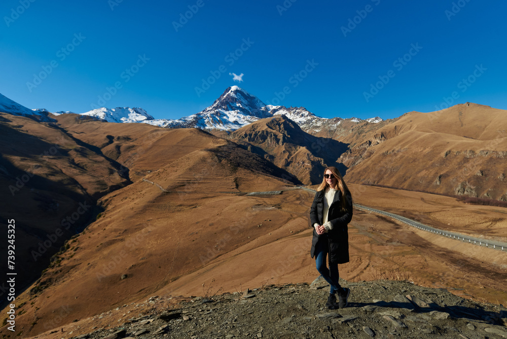 A stunning wooman appreciating the grandeur of the tall brown mountains with white snowy peaks.