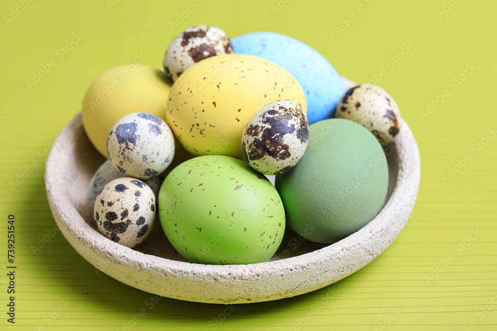 Bowl with Easter eggs on green background.