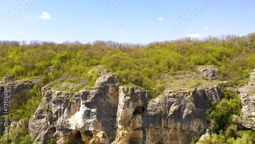 Big rock covered in dense forest, clear sky in background, aerial drone view.