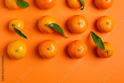 Delicious tangerines and green leaves on orange background, flat lay. Space for text