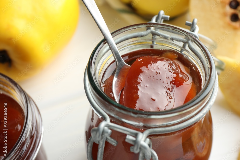 Taking tasty homemade quince jam from jar on blurred background, closeup Taking tasty homemade quince jam from jar on blurred background, closeup