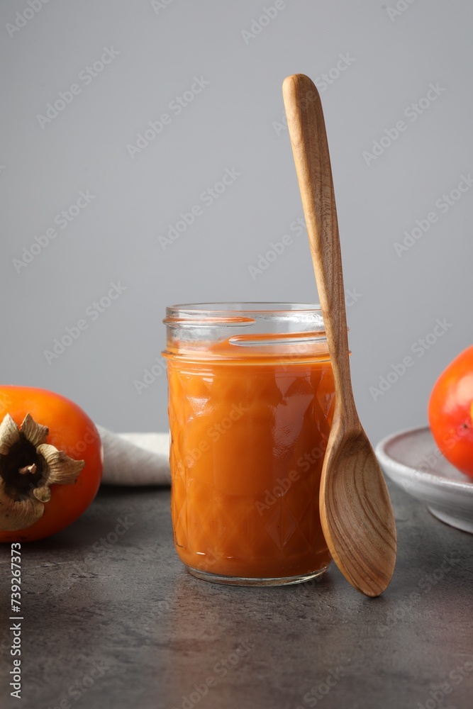 Delicious persimmon jam in glass jar served on gray table Delicious persimmon jam in glass jar served on gray table
