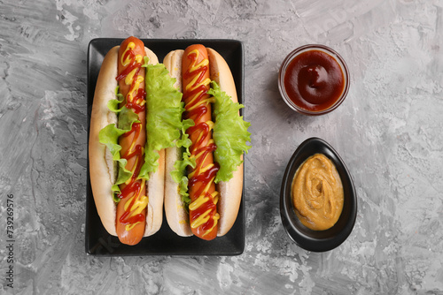 фотографія Tasty hot dogs with lettuce, ketchup and mustard on grey textured table, flat la