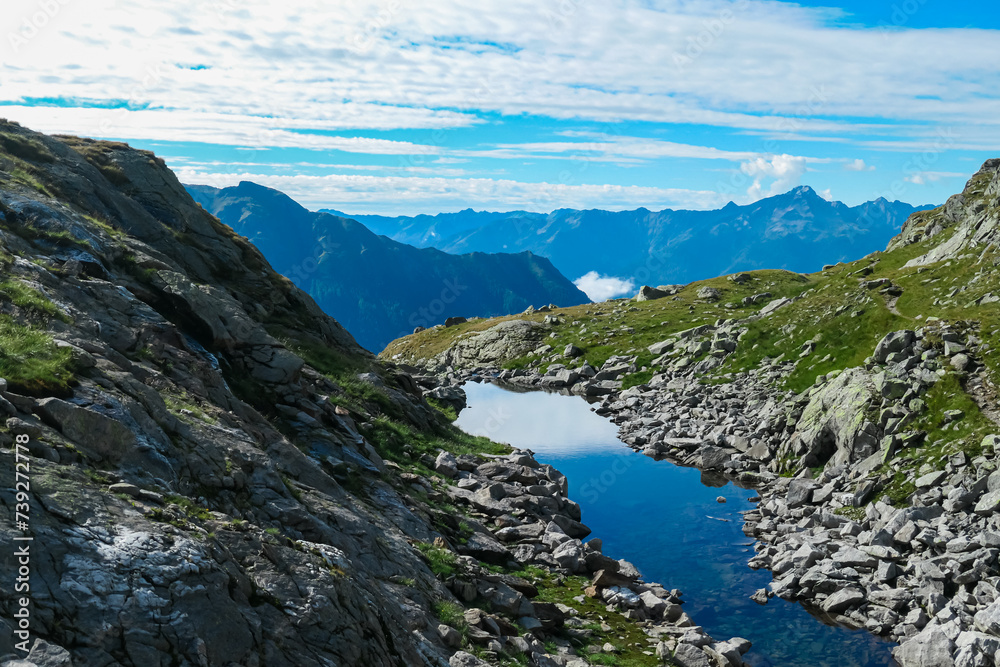 Small high altitude alpine lake surrounded by rocks in High Tauern National Park, Carinthia, Austria. Idyllic hiking trail with panoramic view of mountain ridges in Austrian Alps. Summer in Mallnitz