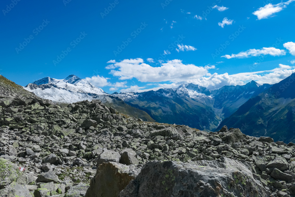 Rock formation with panoramic view of majestic snow covered mountain peaks of High Tauern National Park, Carinthia, Austria. Idyllic hiking trail over rocky scree field in summer. Remote Austrian Alps