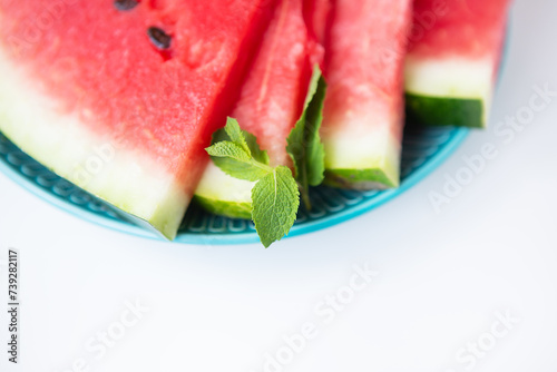 Fresh watermelon slices with mint on a blue plate, isolated on a white background.