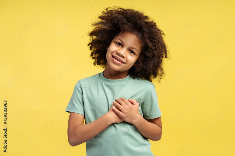 Gleeful little African American girl with curly hair, clasping her hands on her heart in gratitude Gleeful little African American girl with curly hair, clasping her hands on her heart in gratitude