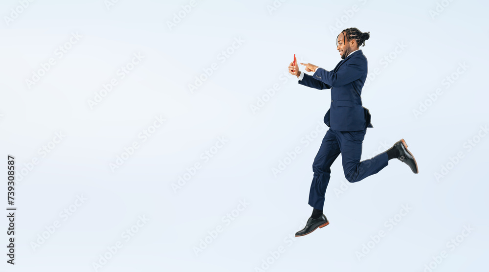 Full body photo of a black businessman jumping while looking at his smartphone. (We also sell PNGs that are cropped and have transparent background. Please search for 