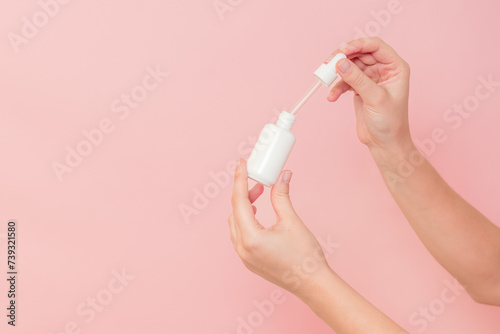 Hand holding glass cosmetic bottle for serum (hyaluronic acid and collagen) on pink background. Beauty concept