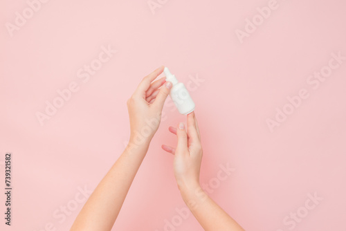 White bottle with serum lotion or essential oil (hyaluronic acid and collagen) in hands on pink background. Skin care cosmetics concept, beauty flyer photo