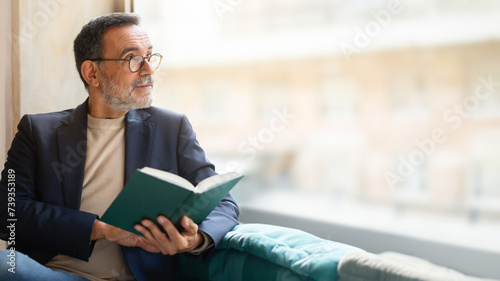 Mature man in glasses engrossed in a book, thoughtful expression photo