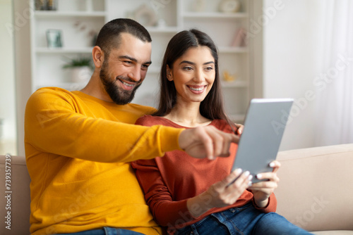 Happy Young Couple Using Digital Tablet While Relaxing At Home Together