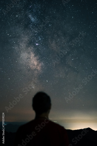 The Milky Way in the night sky and a blurred silhouette of a person standing and looking at it