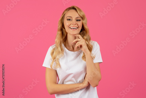 Portrait of happy blonde woman touching chin over pink background