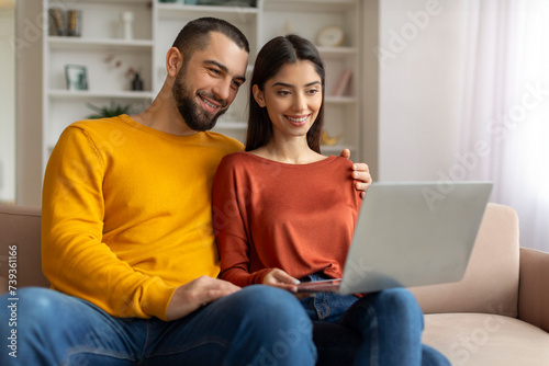 Portrait Of Happy Young Couple Browsing Internet On Laptop At Home