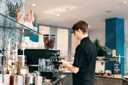 Young barista making coffee at automatic machine in a modern coffee shop. Student working part-time in cafe. Problems of unemployment and Job opportunities for youth. Small business vacancies photo
