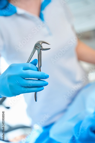 Dentist in protective gloves holds a tool for removing teeth
