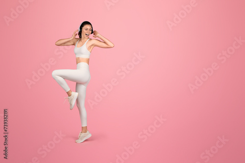 Vibrant and joyful woman in white sportswear dancing or doing aerobics with headphones