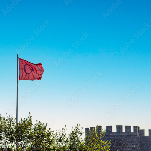 A Turkish flag waves proudly against a clear blue sky atop an ancient stone fortress, symbolizing national pride.Erzurum castle , Turkey.