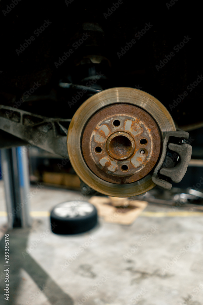 close-up at a service station a car part in a suspended state without wheel a rusty part on the floor wheel