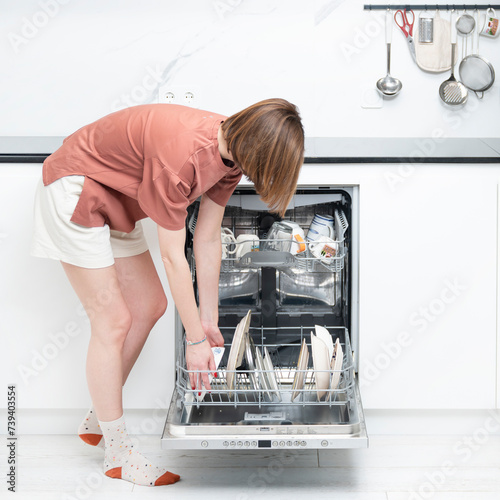 Busy housewife putting dirty plates in dishwasher machine in the kitchen. Household and exhausting cleaning day concept