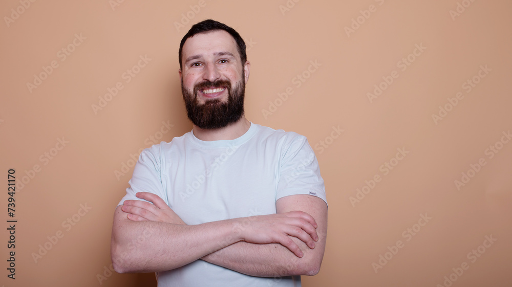 man with a beard is smiling and wearing a white shirt. He is standing in front of a tan wall man with a beard is smiling and wearing a white shirt. He is standing in front of a tan wall