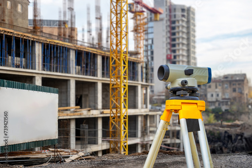 Geodetic instrument. Building under construction. Optical theodolite. Geodetic device on tripod. Construction site without anyone. Equipment for surveyor. Geodetic quality control of construction photo