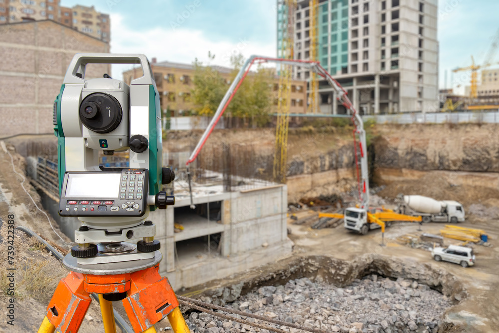 Surveyor equipment at construction site. Geodetic device on tripod. Optical theodolite near house under construction. Electronic surveyor tool. Equipment for measuring work in geodesy - obrazy, fototapety, plakaty 