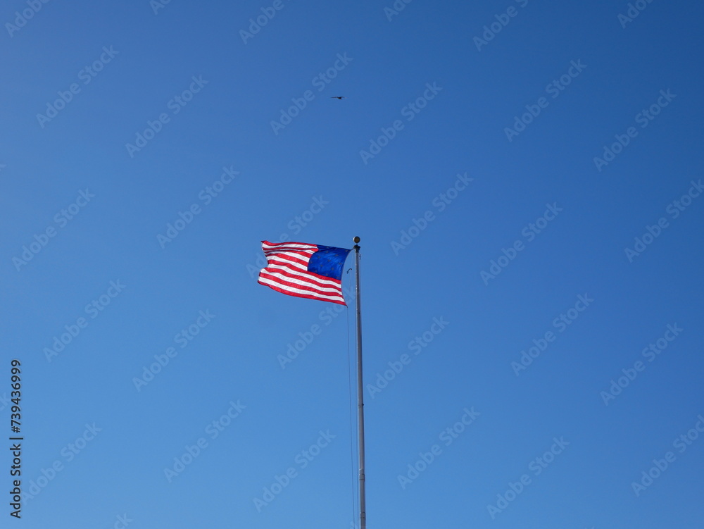 large flag of the united states fluttering into the wind on a blue sky day large flag of the united states fluttering into the wind on a blue sky day
