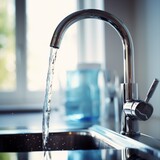 Fresh running water from a modern chrome kitchen faucet for clean hydration. Stream of purity: clear water flowing from a shiny tap in a domestic kitchen setting.