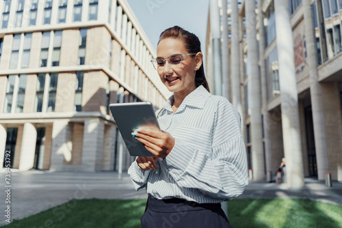 Professional woman using a tablet outdoors, smiling with a modern building in the background.