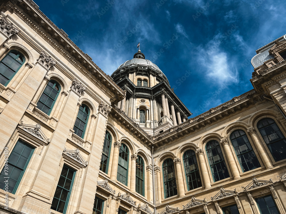 Rear views of the Illinois State Capitol Building in Springfield, Illinois, USA. Cloudy blue skies overhead. The US flag, State of Illinois Flag, and Black History Month Flag fly atop the dome. Rear views of the Illinois State Capitol Building in Springfield, Illinois, USA. Cloudy blue skies overhead. The US flag, State of Illinois Flag, and Black History Month Flag fly atop the dome.