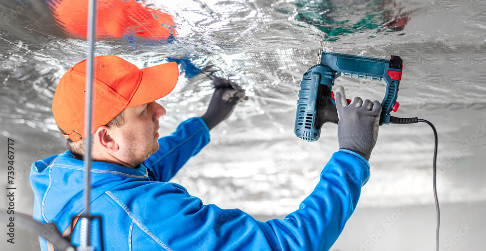 The builder is fastening the vapor barrier under the ceiling thermal insulation using an