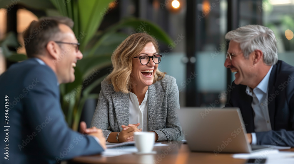 A smiling woman holding a pen is enjoying a light-hearted moment with her colleagues in a sunlit, modern office space.