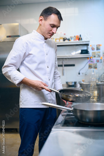 Young male chef cooks on a frying pan