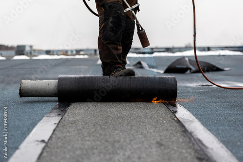 professional roofer at work securing rolled tar paper with a blowtorch on a flat roof installation process photo