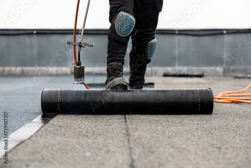 professional roofer applying bitumen roll on flat roof with a gas burner at a modern construction site photo