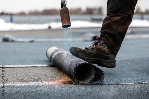 professional roofer at work securing rolled tar paper with a blowtorch on a flat roof installation process photo