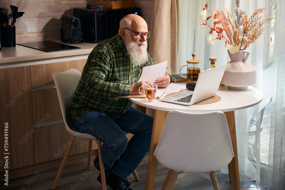 Pensioner works at the kitchen table on a laptop Pensioner works at the kitchen table on a laptop