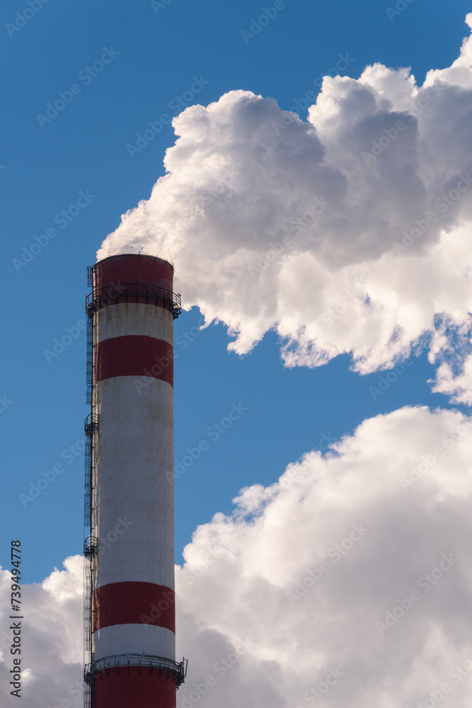Industrial pollution of the environment. Plumes of white smoke from a chimney against a blue sky background, vertical frame. Industrial pollution of the environment. Plumes of white smoke from a chimney against a blue sky background, vertical frame.