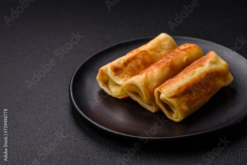 Delicious fried pancakes with filling rolled on a dark concrete background