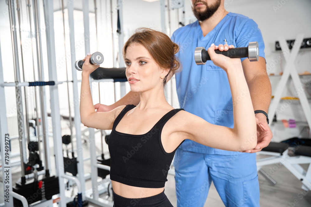 Woman performs exercises with dumbbells under supervision of physiotherapist Woman performs exercises with dumbbells under supervision of physiotherapist
