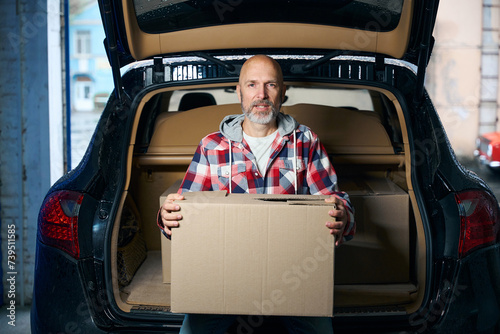 A man sits on the open trunk of a car