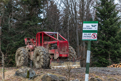 Tabliczka informacyjna "TEREN MONITOROWANY" oraz "SKŁAD DREWNA" na tle maszyny leśnej do wyciągania drewna z lasu.