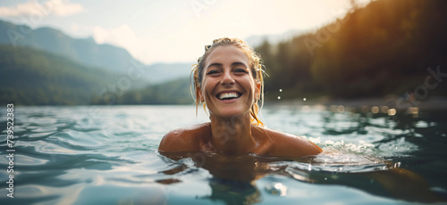 a mature, happy woman joyfully swims in the crystal-clear lake on a warm summer day, with the sun glistening on the water's surface © Christophe