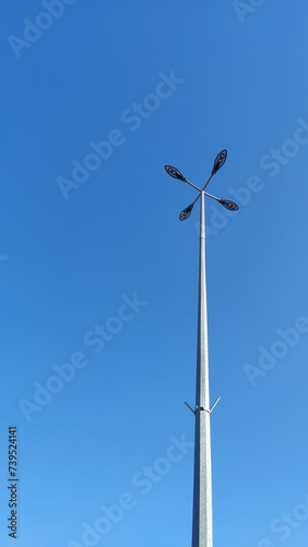 Lighting pole with four lamps against a background of blue sky in sunny weather. Urban electro-energy technologies. Savings on street urban lighting. Minimalism