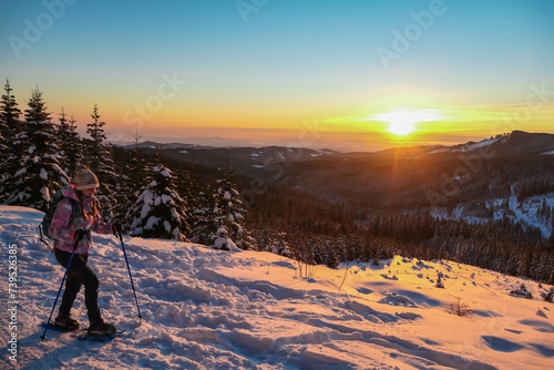 Sport woman in snow shoes enjoying beautiful sunrise over alpine landscape of Kor Alps, Carinthia Styria, Austria. Tranquil serene atmosphere in winter wonderland, Austrian Alps. Idyllic hiking trail