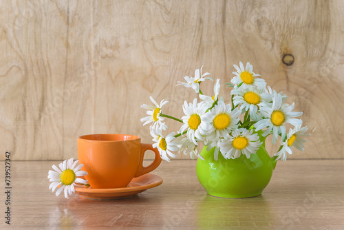 Fototapeta Naklejka Na Ścianę i Meble -  Summer morning breakfast concept; orange cup of coffee and bouquet of white daisies on a wooden background