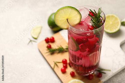 Tasty cranberry cocktail with rosemary and lime in glass on gray table, closeup. Space for text