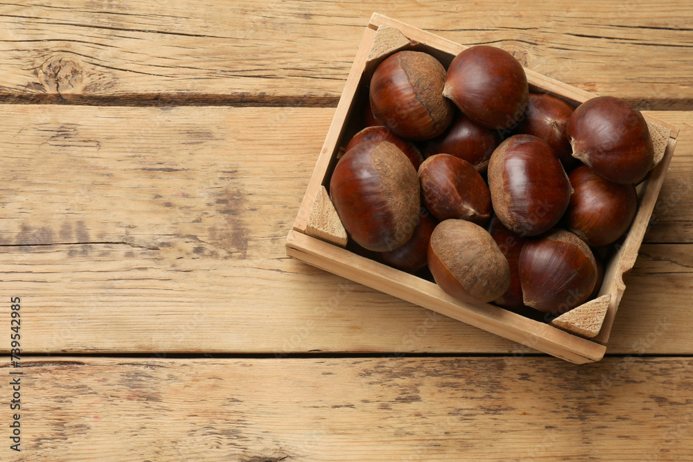 Sweet fresh edible chestnuts in crate on wooden table, top view. Space for text Sweet fresh edible chestnuts in crate on wooden table, top view. Space for text